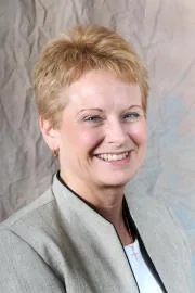 Short blonde hair woman with warm smile wearing gray blazer and dark collar